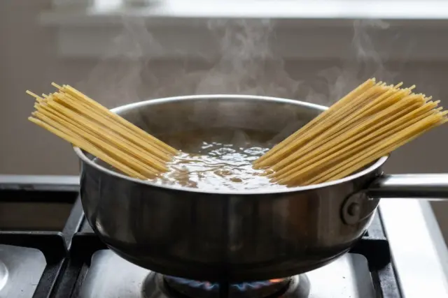 A pot of boiling water on a kitchen stove with long dry spaghetti noodles sliding gently under the bubbling surface